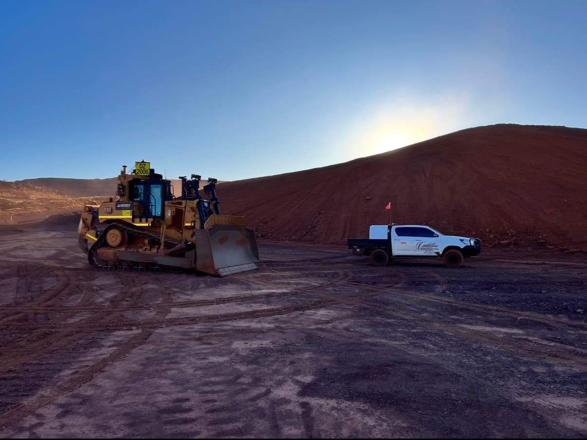 CAT dozer and a signwritten Cadillac Contracting and Civil ute on a bulk earthworks site at golden hour