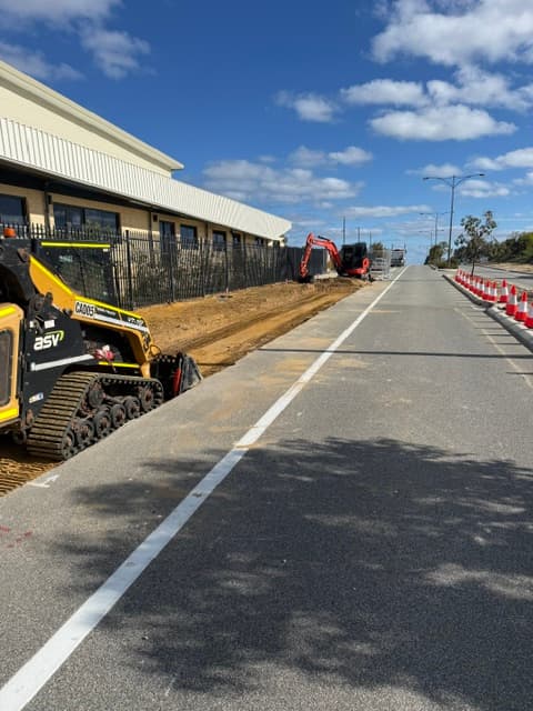 Skid steer working along a road verge with an excavator further down the line